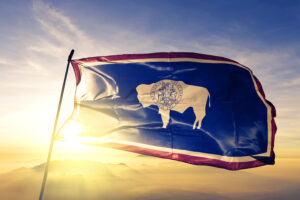 Wyoming state of United States flag on flagpole textile cloth fabric waving on the top sunrise mist fog